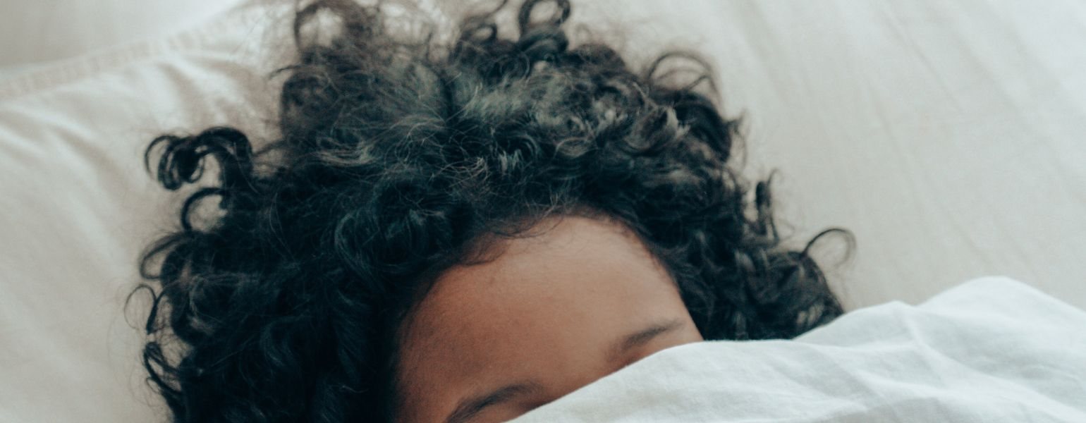 Woman with black curly hair hiding under the duvet