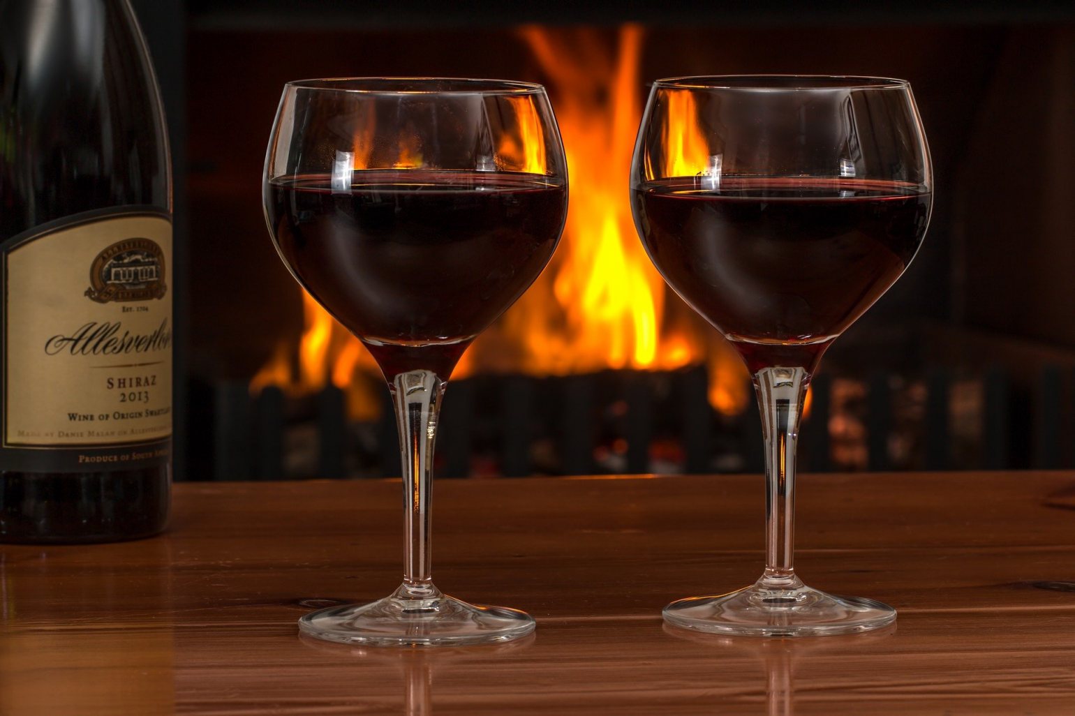 two glasses of red wine by a fireplace