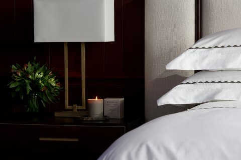 Luxury bedroom setting with a glowing wildsmith candle and flowers on the bedside table, clean crisp Reed Family Linen white bed linen covers the bed, behind sits a white, custom-made Vispring headboard - The Sleep Well Collection Giveaway with Wildsmith Skin and Reed Family Linen 