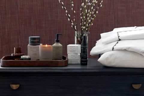 Luxury Wildsmith bathroom and skin products, lit candle and Reed Family Linen set on top of a dark wooden chest of drawers - The Sleep Well Collection Giveaway Bundles with Wildsmith Skin and Reed Family Linen 