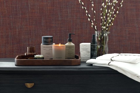 Luxury Wildsmith bathroom and skin products, lit candle and Reed Family Linen pillow cases and duvet cover set on top of a dark wooden chest of drawers - The Sleep Well Collection Giveaway Bundles with Wildsmith Skin and Reed Family Linen 